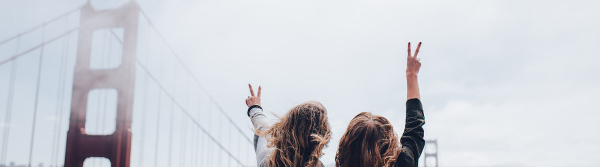 Two girls throwing peace signs by the Golden Gate Bridge.